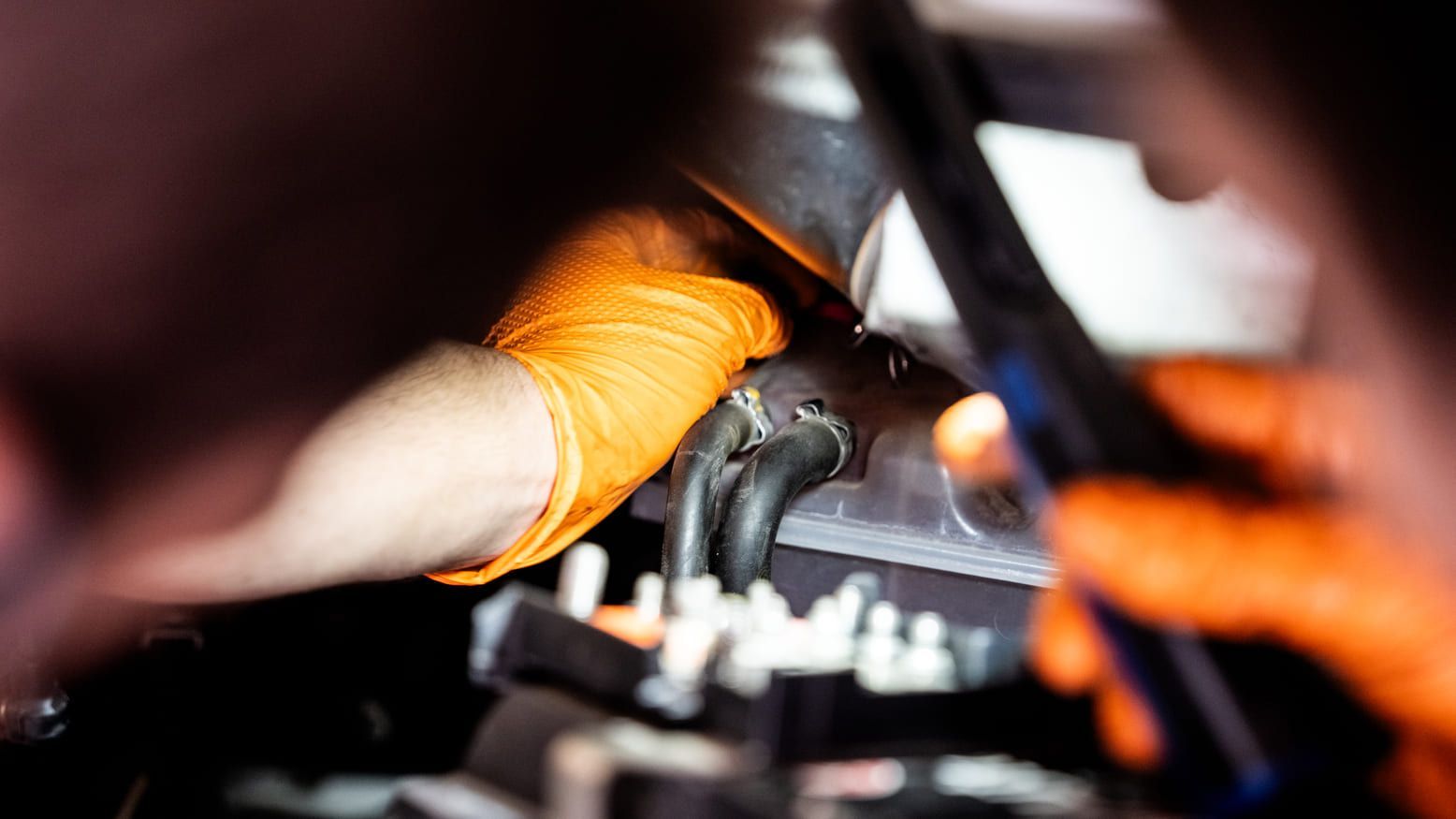 Un hombre que lleva guantes naranjas está trabajando en el motor de un coche.