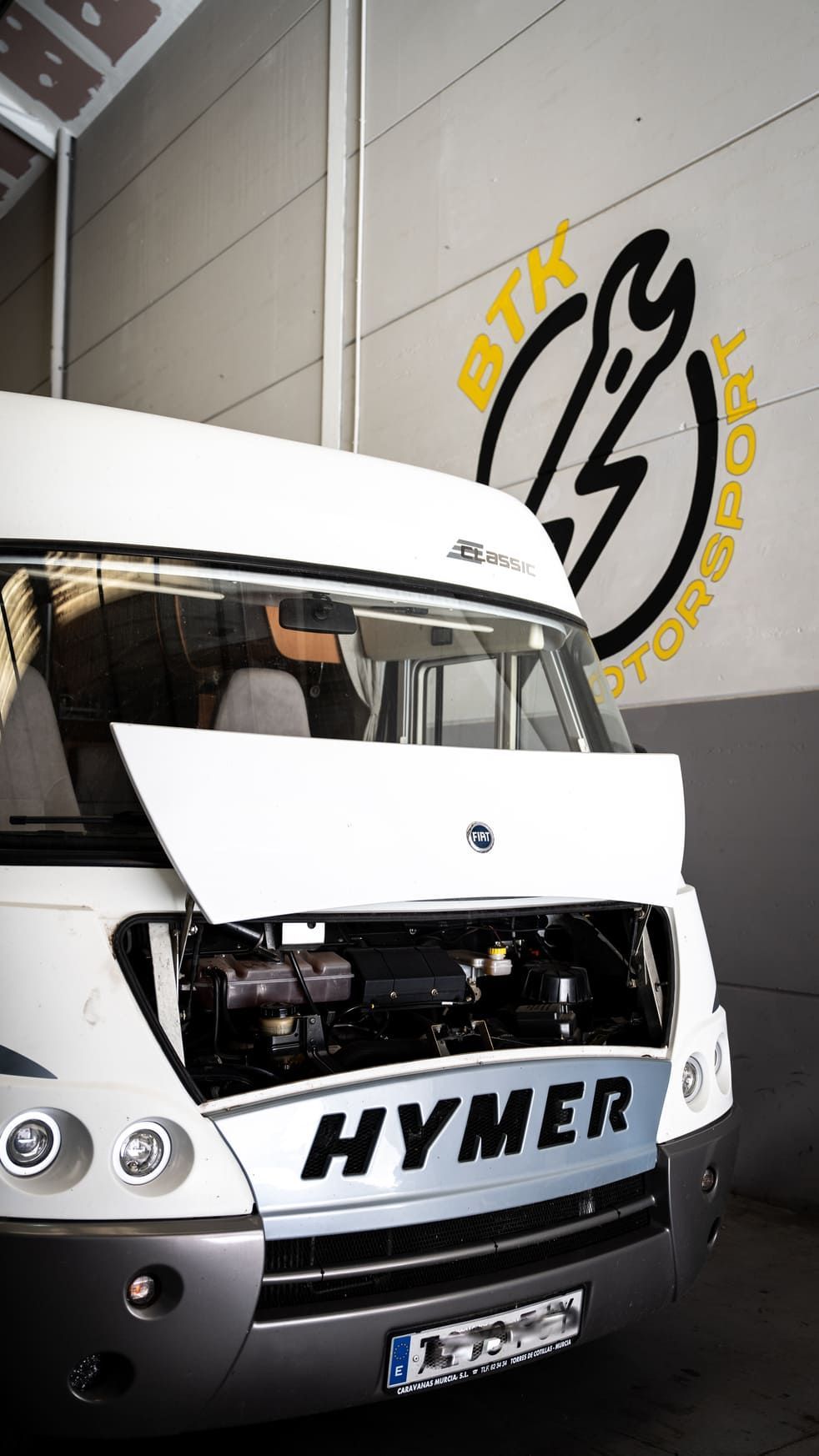 Una furgoneta blanca con el capó abierto está aparcada en un garaje.