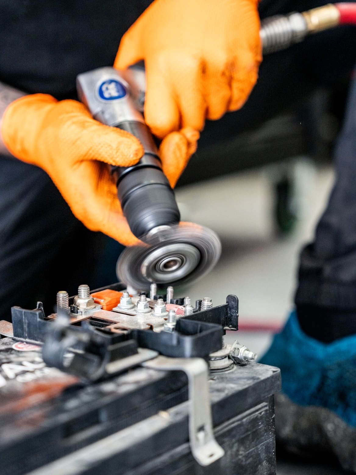 Una persona que lleva guantes de color naranja está trabajando en una batería con una amoladora.