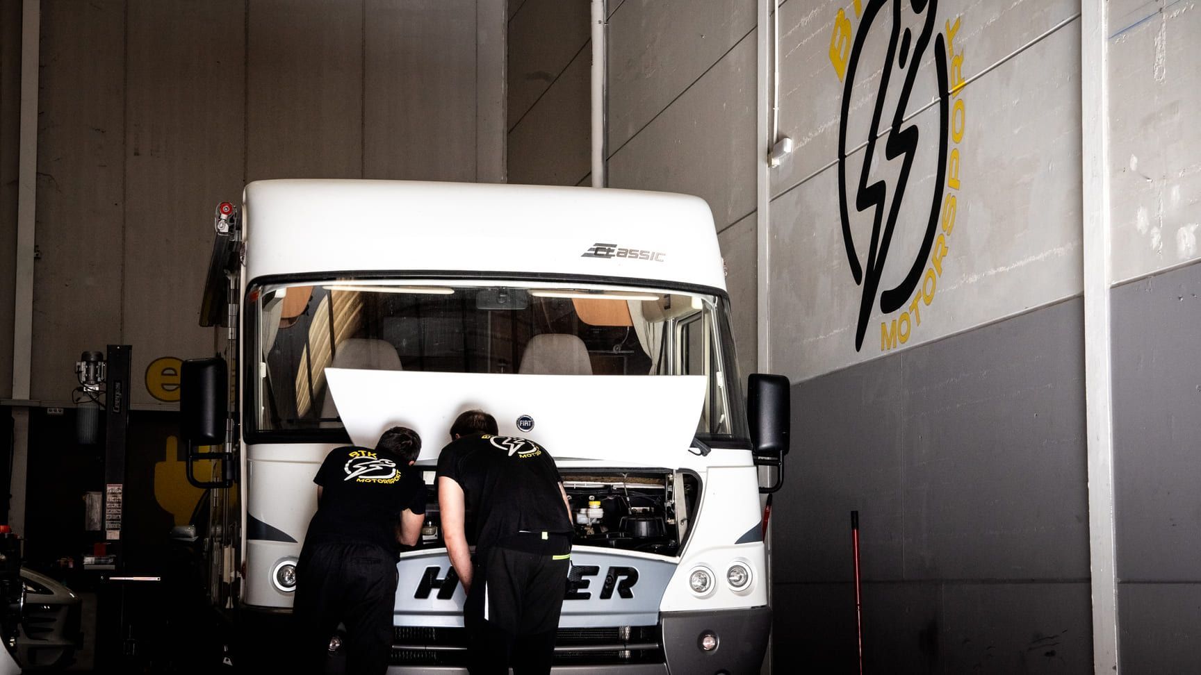 Dos hombres están trabajando en una autocaravana en un garaje.