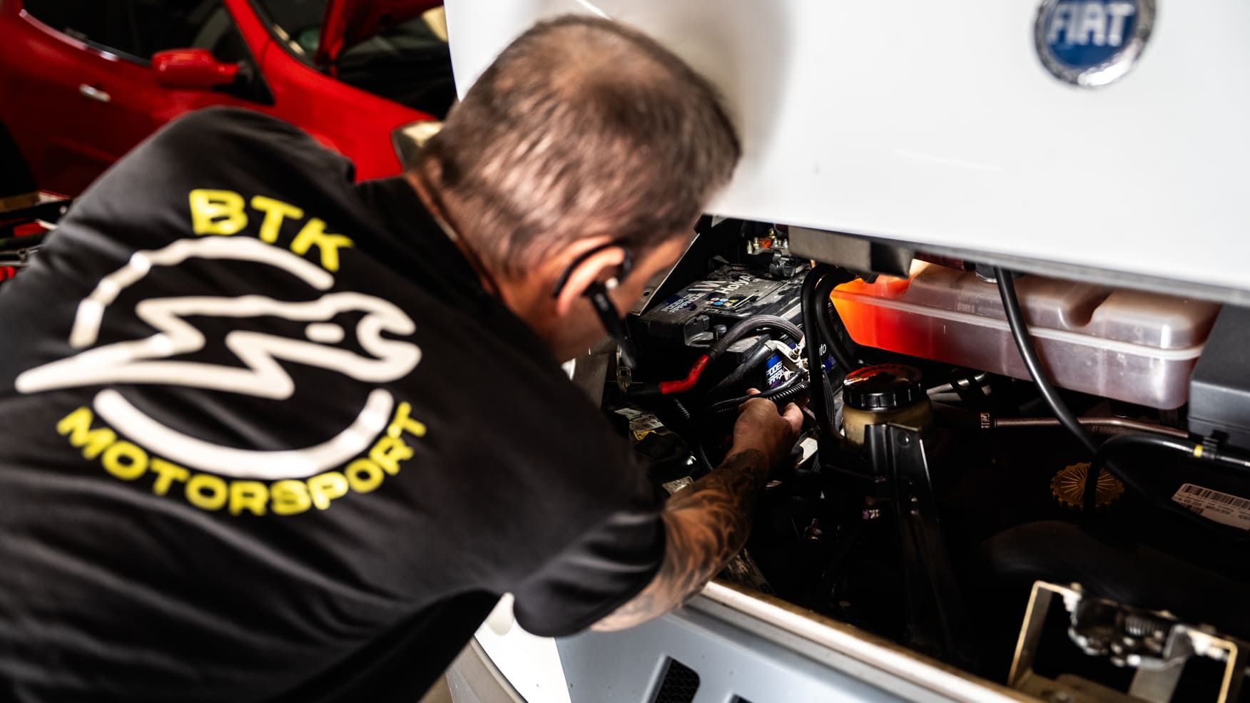 Un hombre que viste una camiseta de BTK Motorsport está trabajando en el motor de un automóvil.