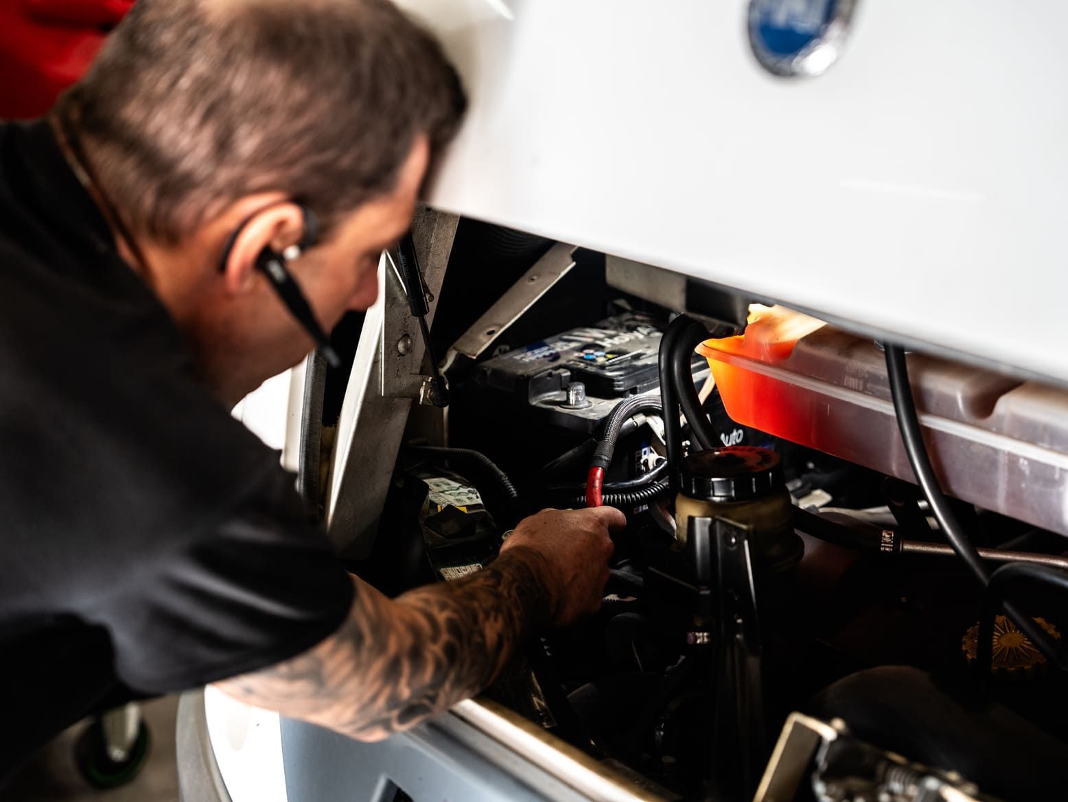 Un hombre está trabajando en el motor de un barco mientras usa unos auriculares.