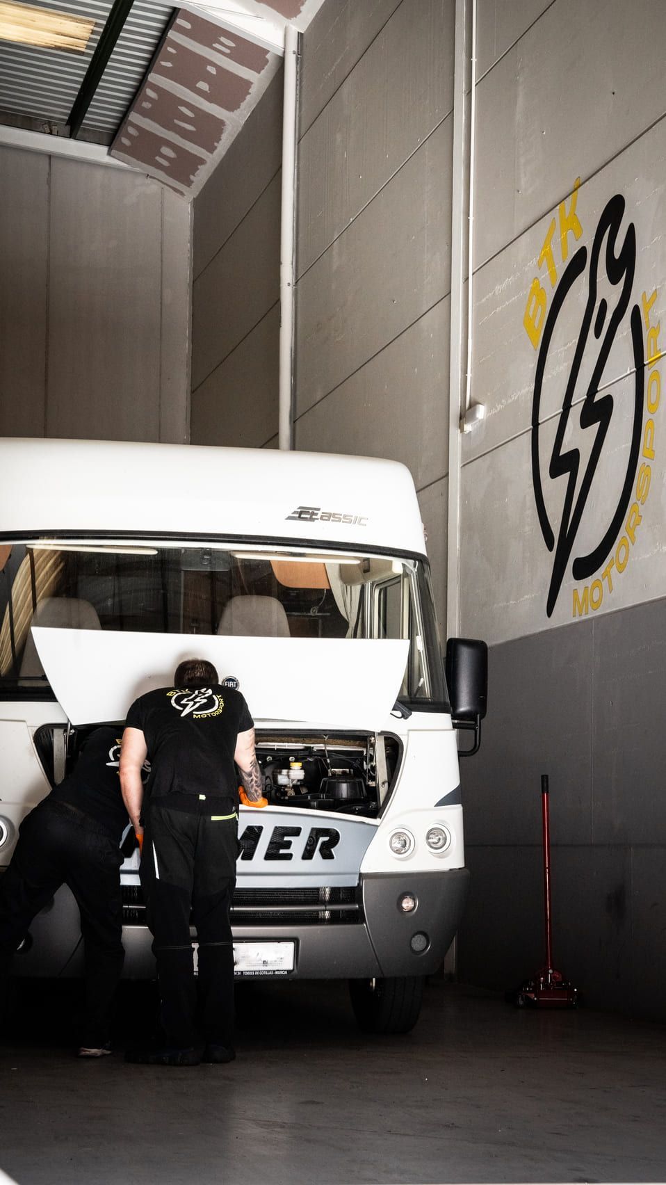 Dos hombres están trabajando en una autocaravana en un garaje.