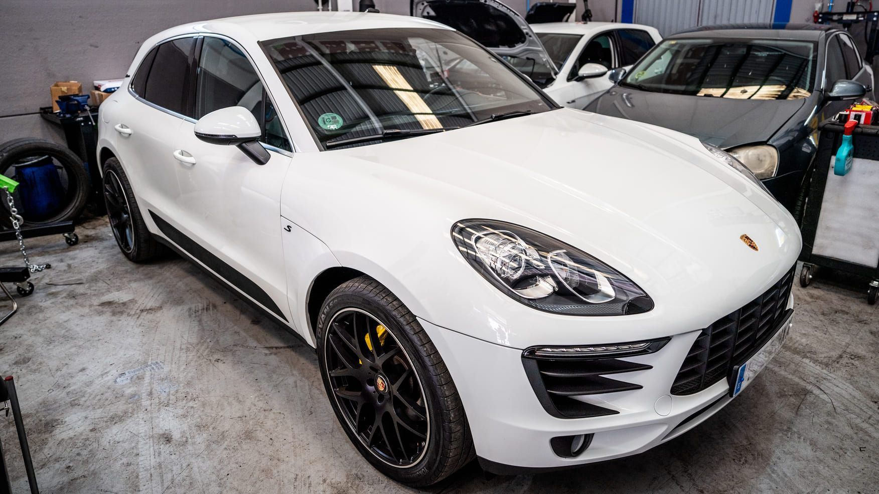 Un Porsche Macan Turbo blanco está aparcado en un garaje junto a otros coches.