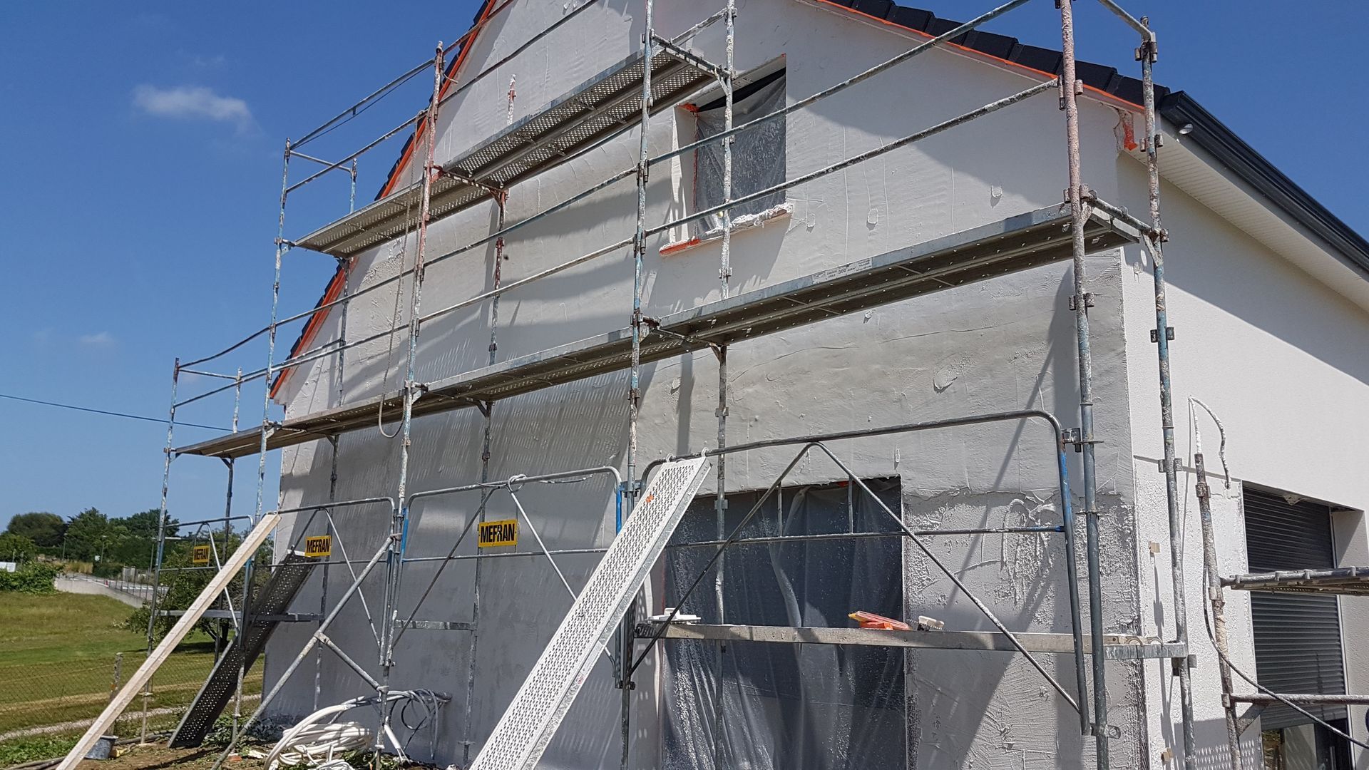 Maison à étage avec un mur jaune, et un toit sombre se détachant sur un ciel bleu