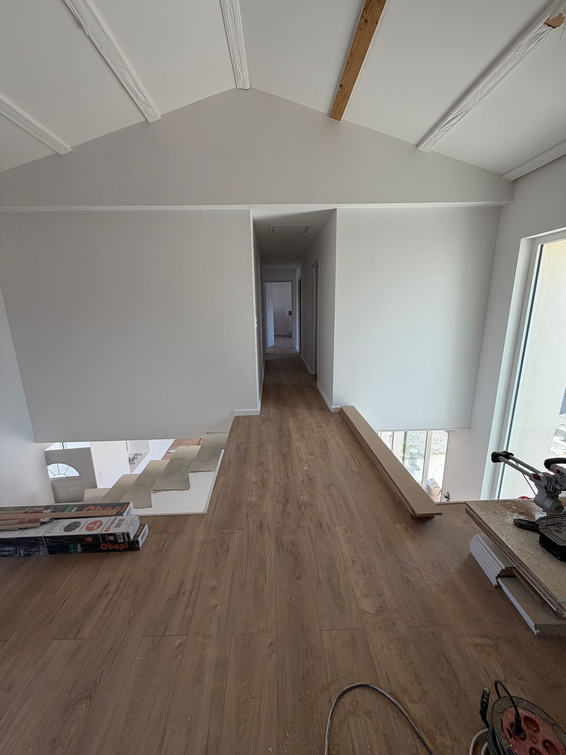 Grenier inachevé avec parquet, murs blancs, poutres apparentes et une ouverture étroite dans le couloir