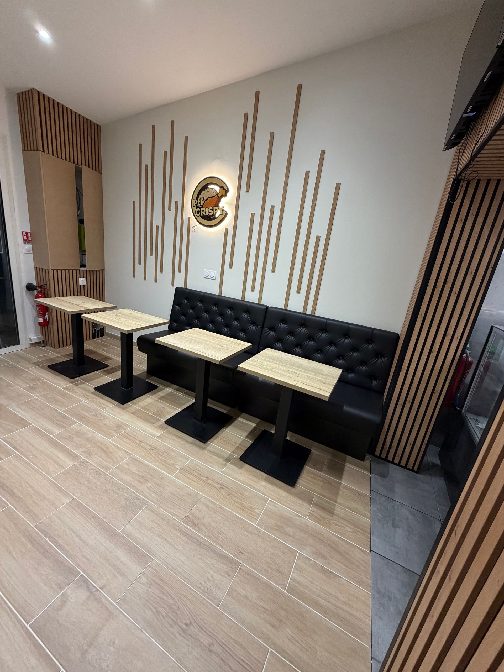 Coin salon de café moderne avec banquette capitonnée noire, tables en bois clair et lambris décoratifs sous un éclairage chaleureux