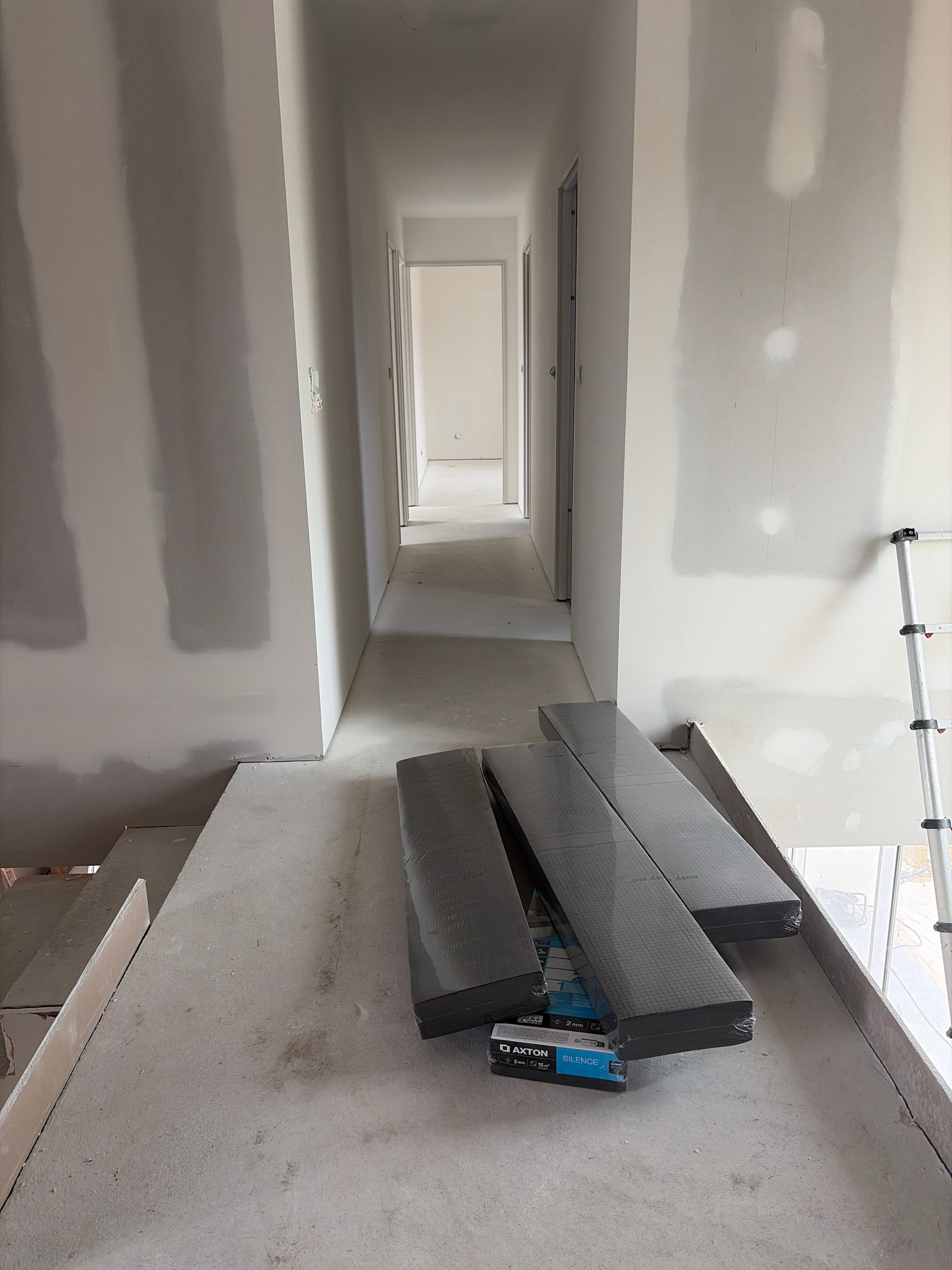 Couloir inachevé avec cloisons sèches, une table de travail et des poutres métalliques empilées au premier plan.