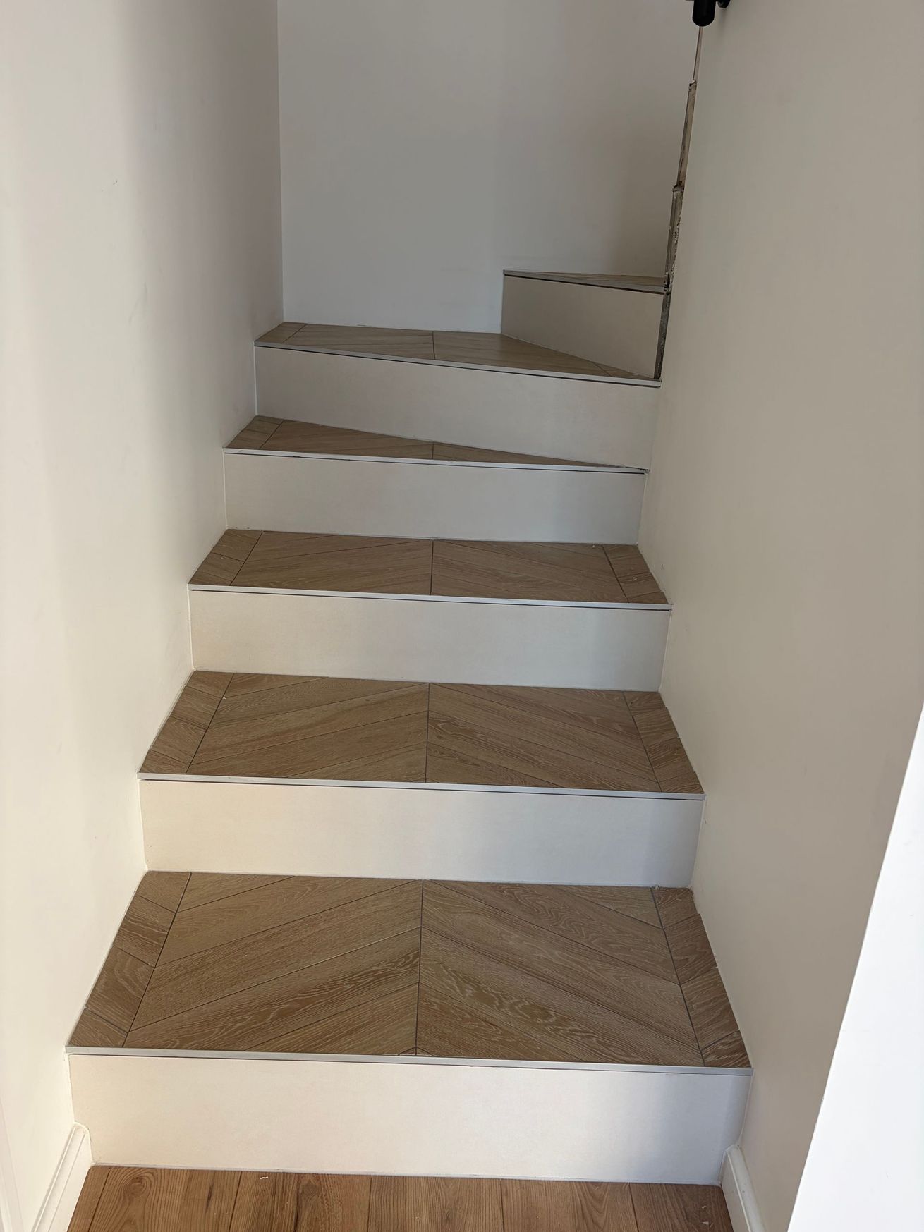 Escalier intérieur étroit avec marches en bois et contremarches blanches, vu vers le haut entre des murs blancs unis