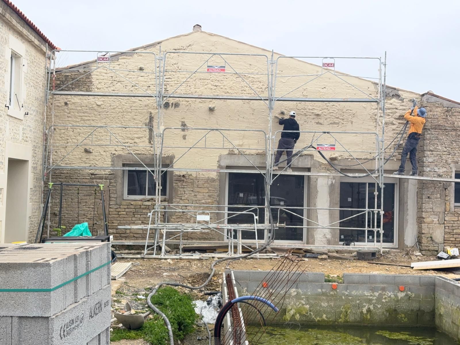 Ravalement de façade d'une maison, avec des échafaudages et des échelles tout autour des murs.