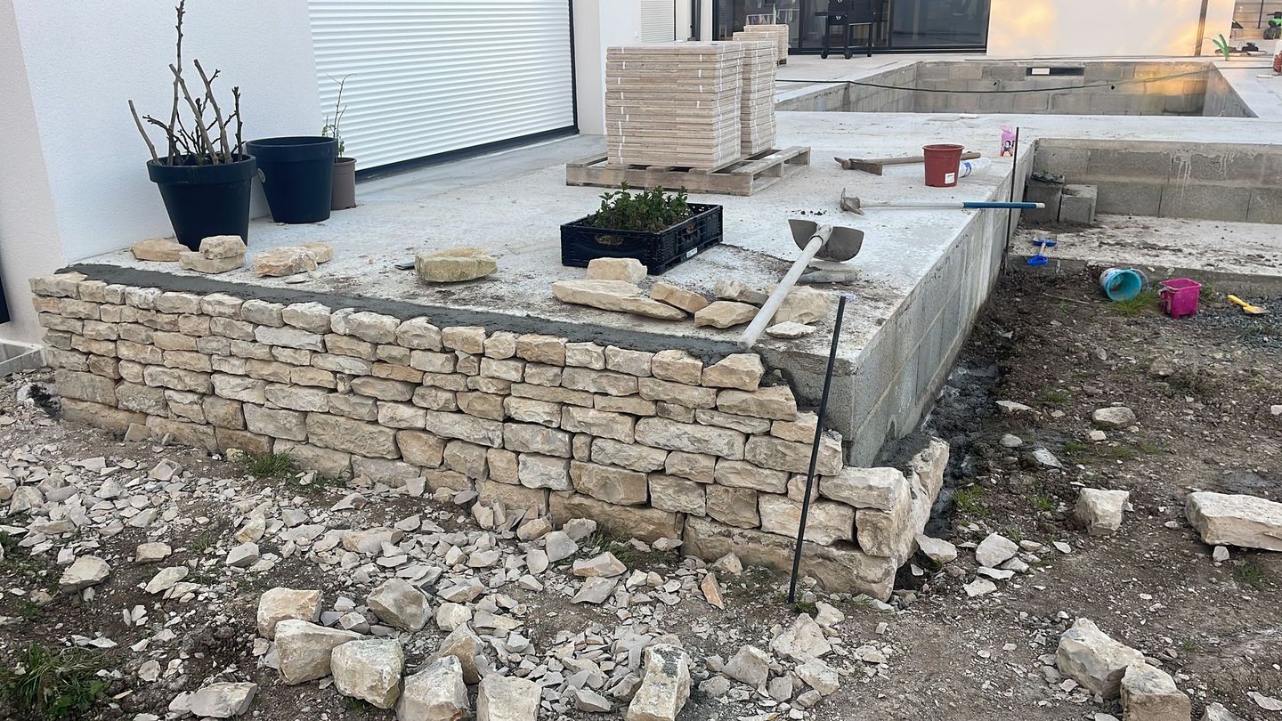 Deux ouvriers dans un bâtiment poussiéreux et inachevé, avec des échafaudages et des colonnes de béton apparentes.