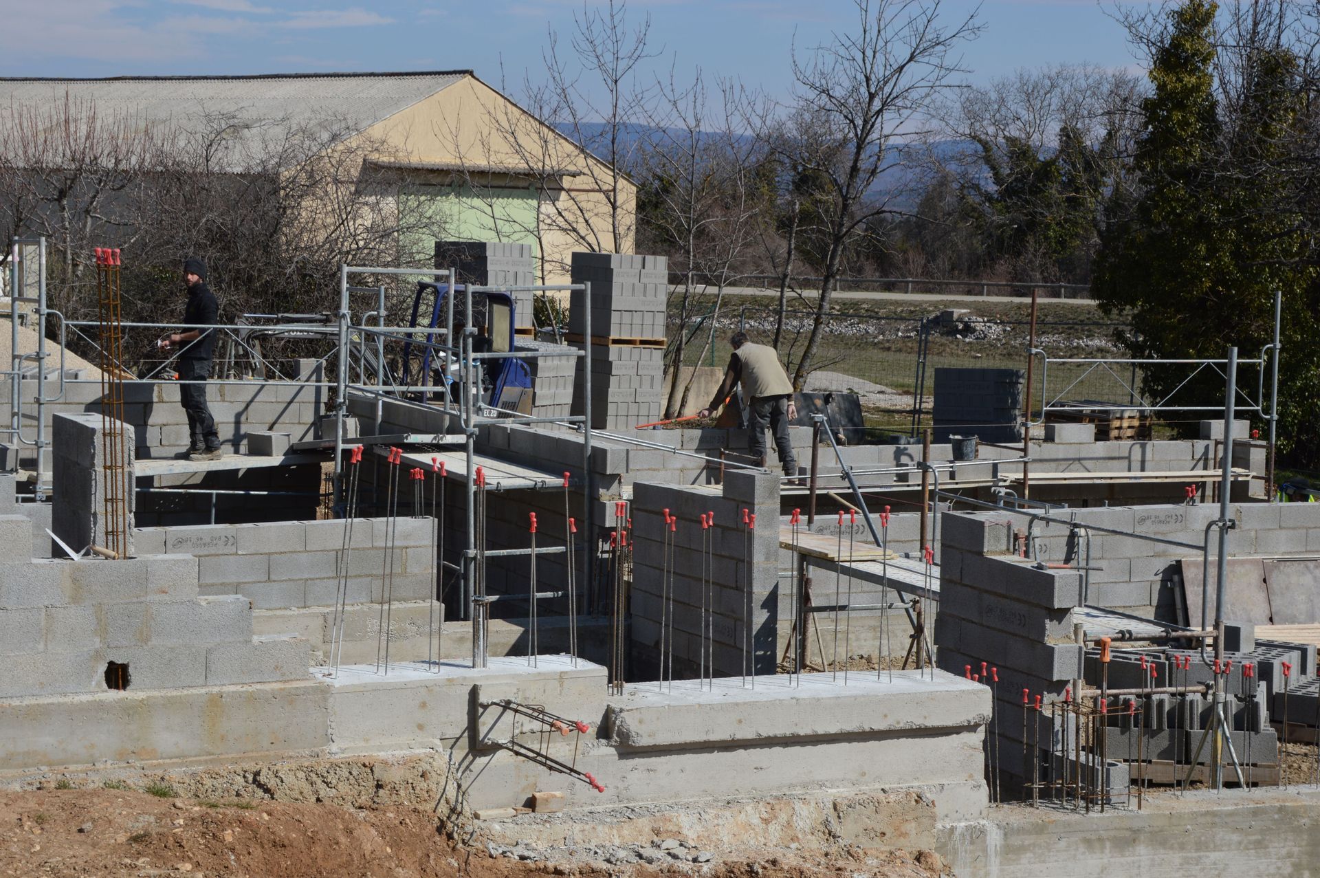 Des ouvriers construisent des fondations en blocs de béton sur un chantier de construction sous un ciel dégagé