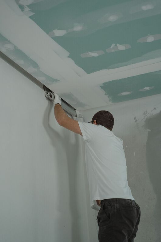 Un ouvrier ponce les joints de plaques de plâtre au plafond d'une pièce en rénovation