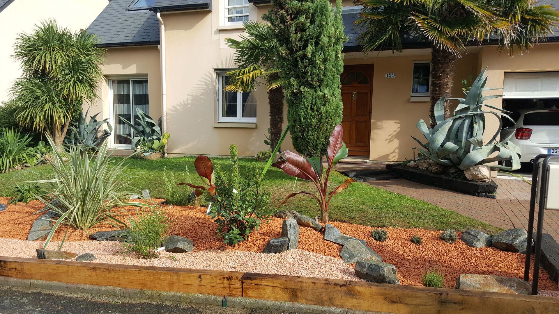 Un jardin avec des plantes et des pierres décoratives devant une maison.
