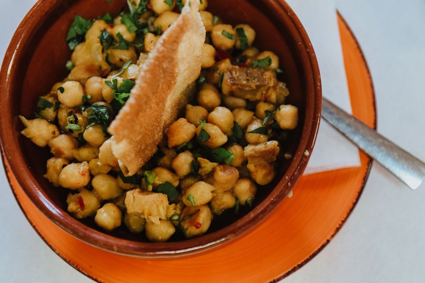 Un bol de garbanzos con un trozo de pan en un plato con un tenedor.