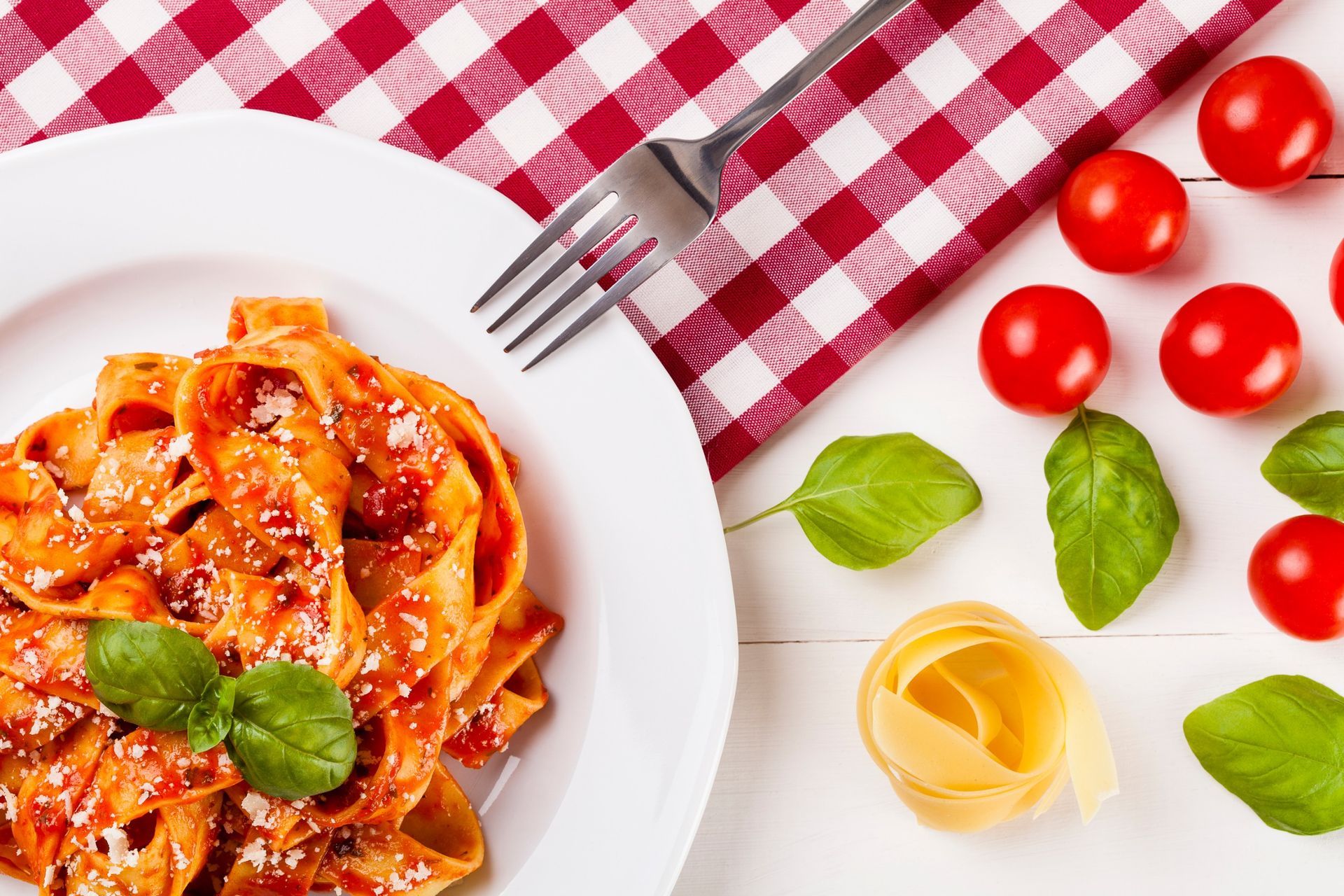 Un plato de pasta con salsa de tomate y albahaca junto a un tenedor y tomates.