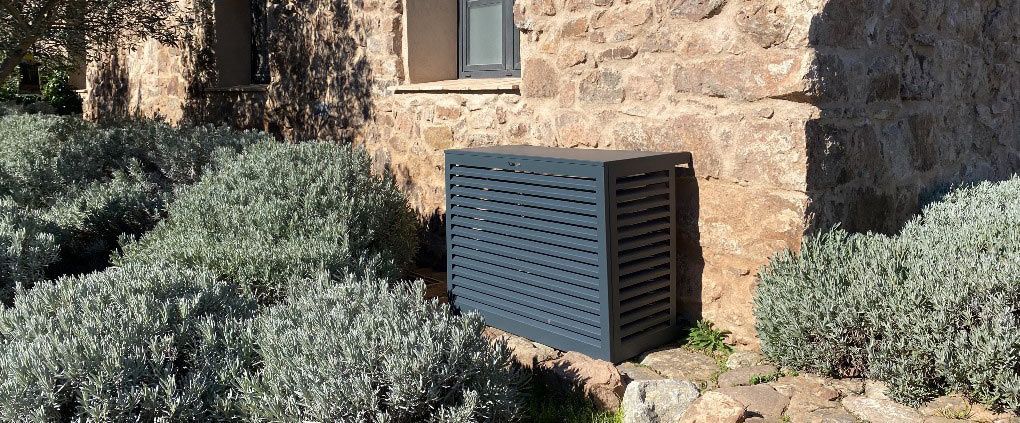 Pompe à chaleur dans un cache noir contre un mur en pierre