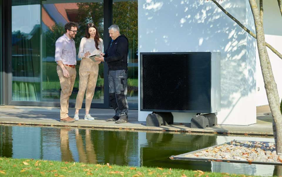 Professionnel faisant signer un contrat à un couple près d'une pompe à chaleur à l'extérieur d'une maison