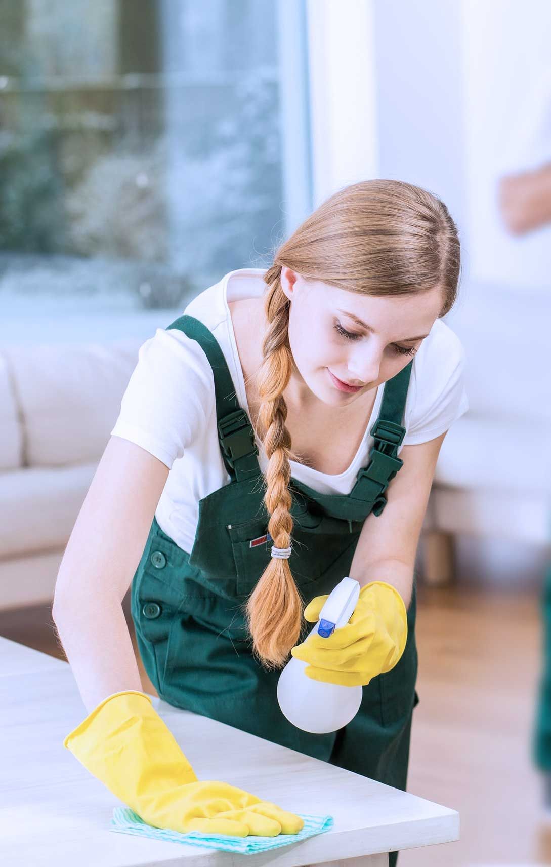Una mujer está limpiando una mesa con una botella de spray y un paño.