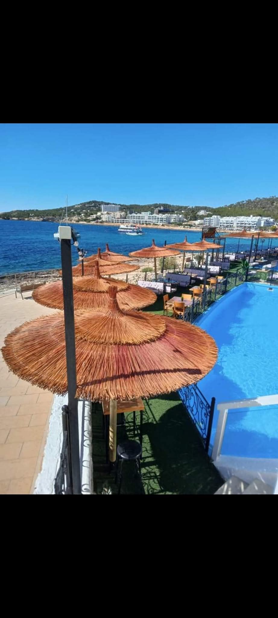 Una hilera de sombrillas de paja en una playa junto a una piscina.