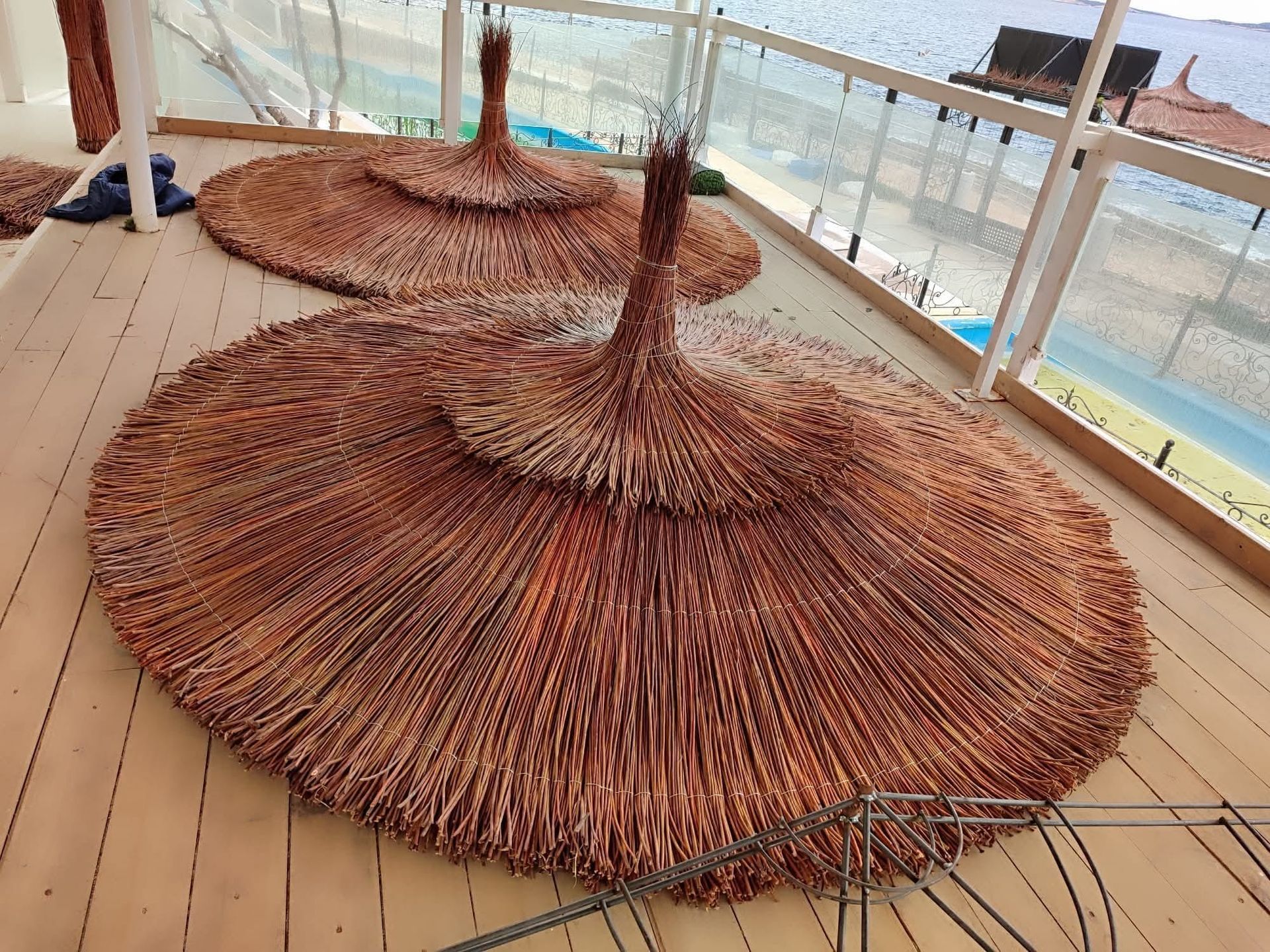 Tres sombrillas de paja están colocadas sobre una terraza de madera.