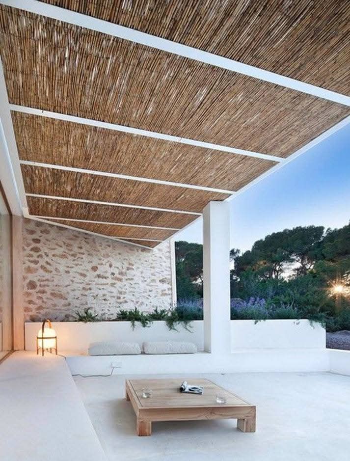 Un patio con techo de paja y una mesa de madera debajo.