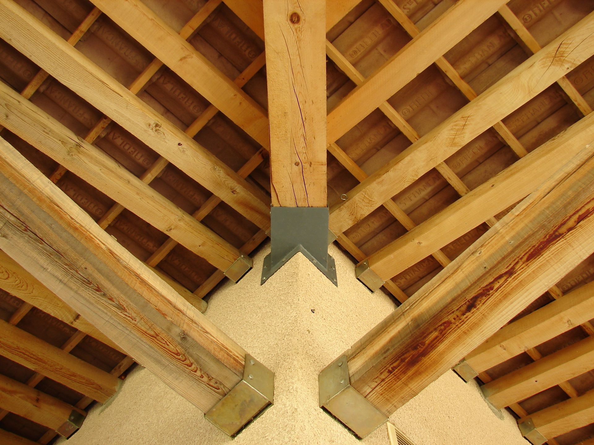 Charpente en bois avec une poutre centrale, fixée par un support métallique.