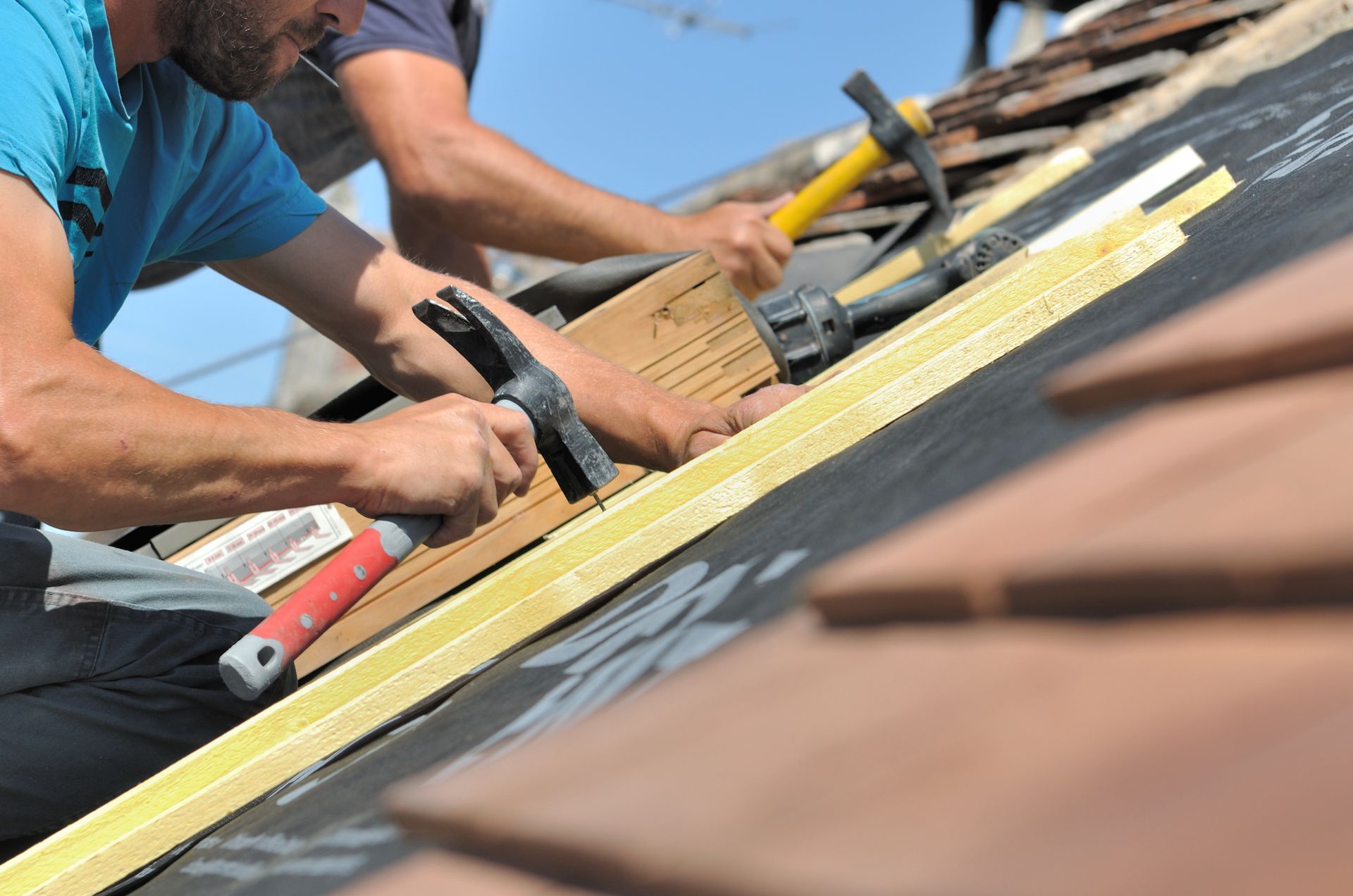 Des couvreurs munis de marteaux qui fixent des liteaux en bois sur une toiture.
