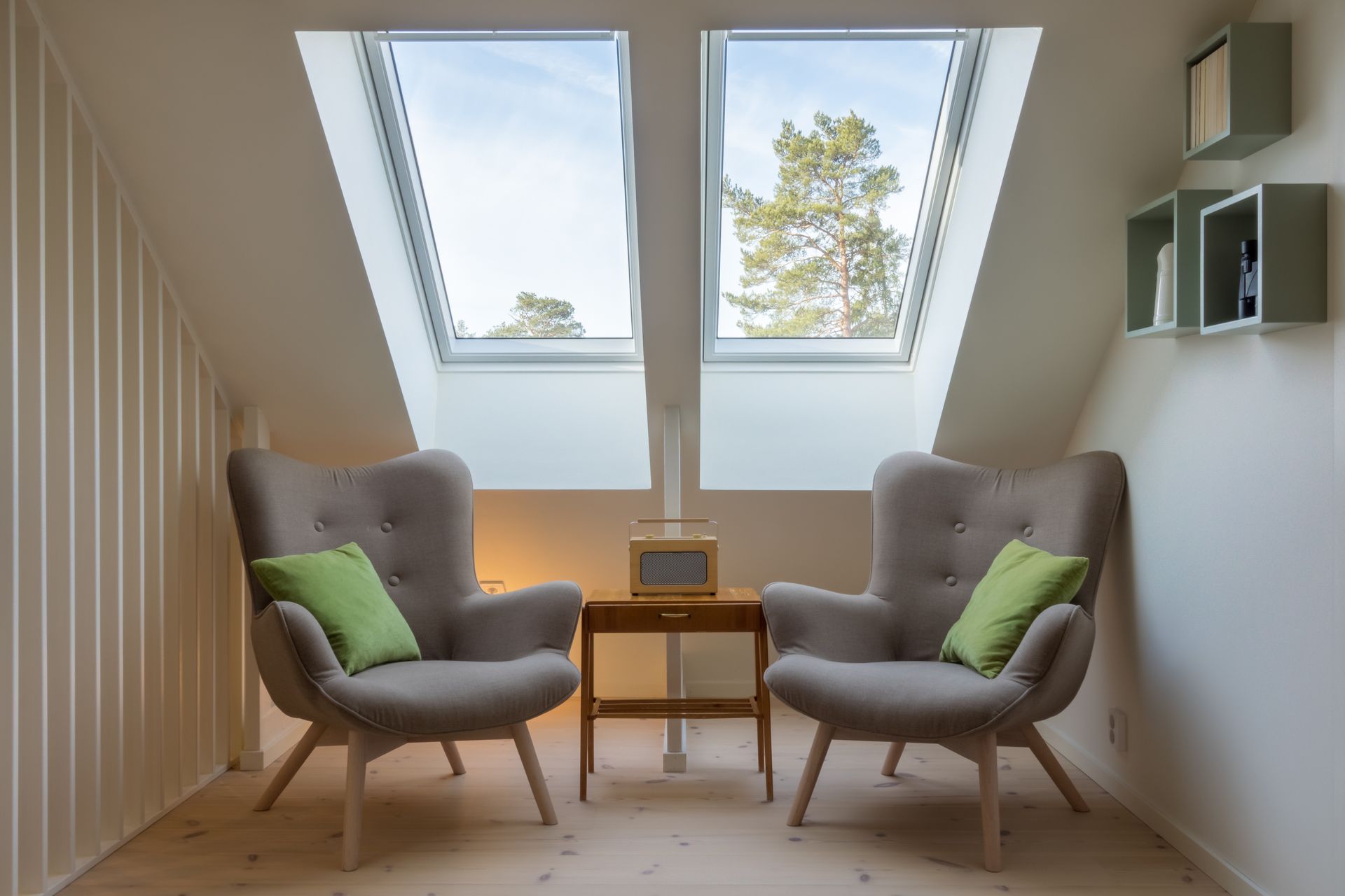 Une pièce mansardée avec une petite table et deux fauteuils, en-dessous de deux fenêtres de toit.