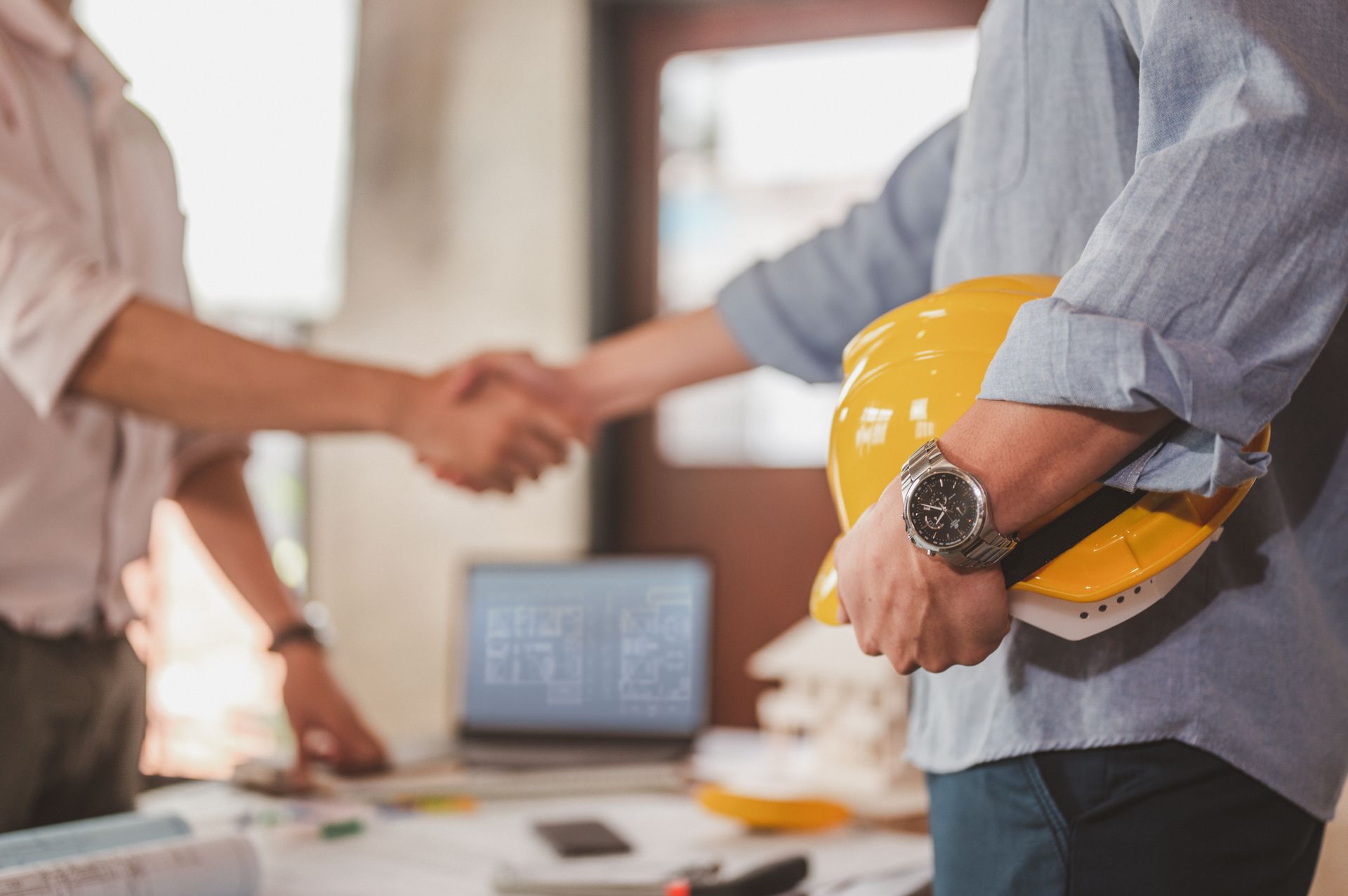 Une poignée de main entre un client et un ouvrier tenant un casque de chantier.
