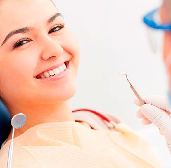 Una mujer sonríe mientras un dentista le examina los dientes.