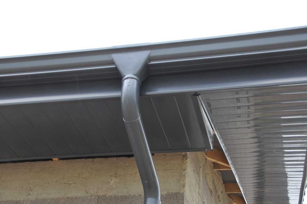 Gouttière et descente pluviale grises sur un débord de toit.