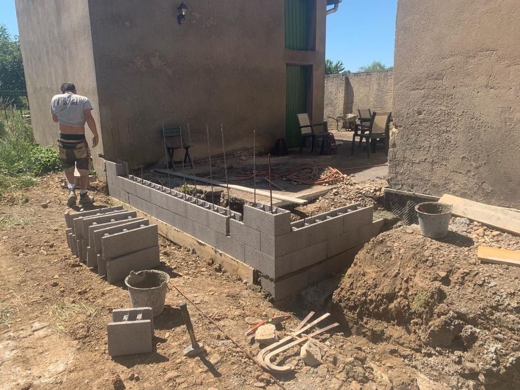 Construction d'un muret en parpaings contre un bâtiment. Une personne est présente.