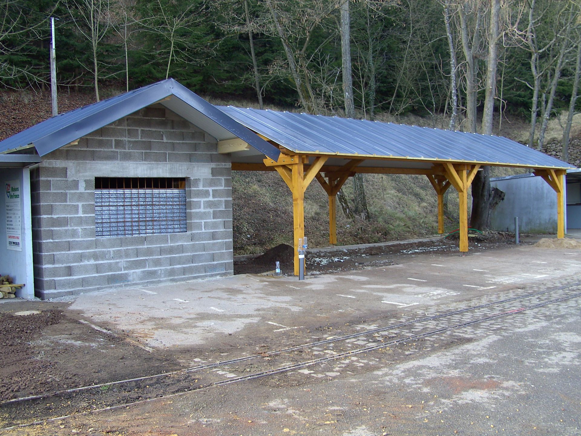 Bâtiment à structure en parpaings et long abri couvert avec des supports jaunes.