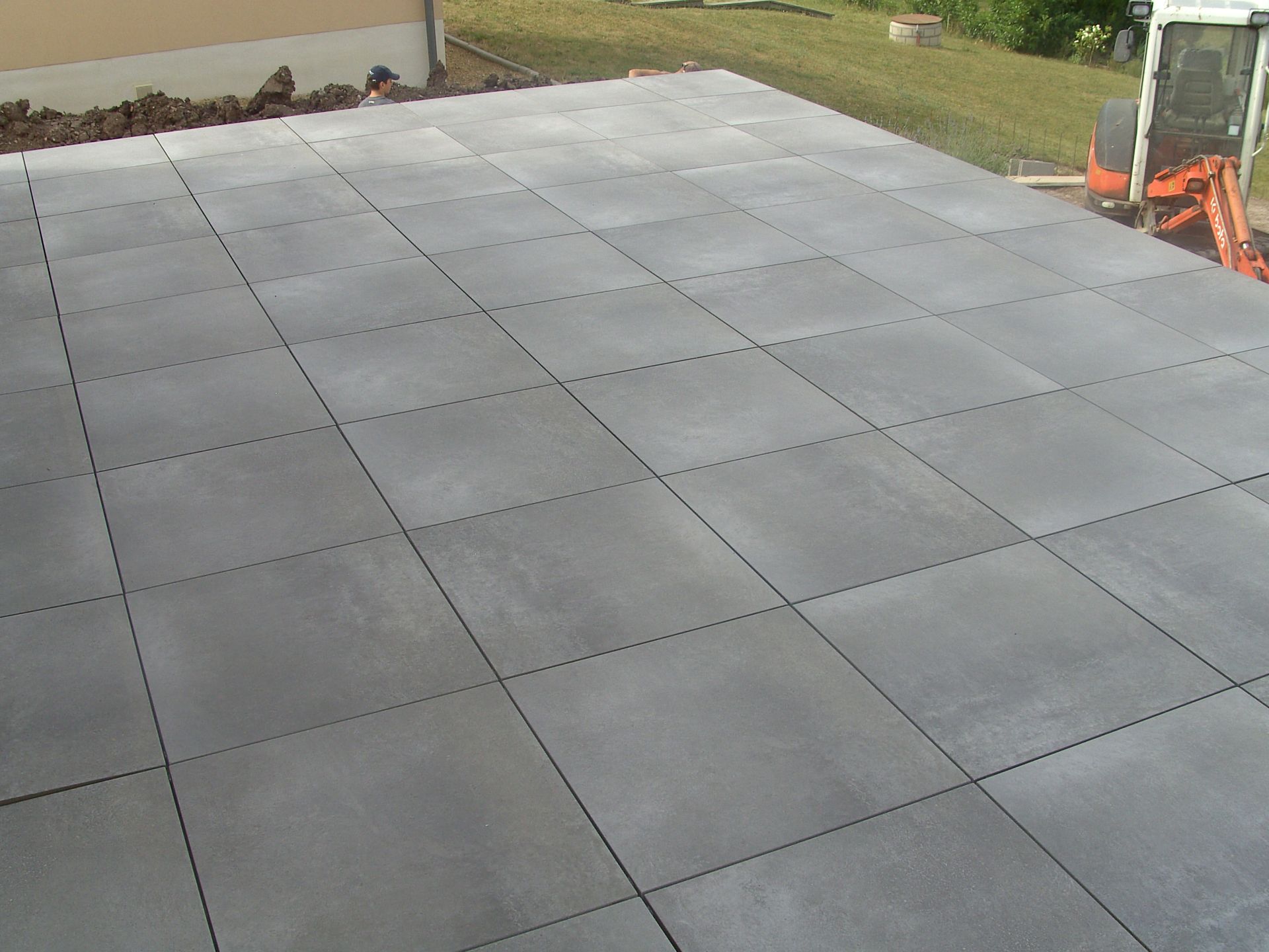 Des dalles carrées en béton gris, posées en damier, créent une surface de terrasse.