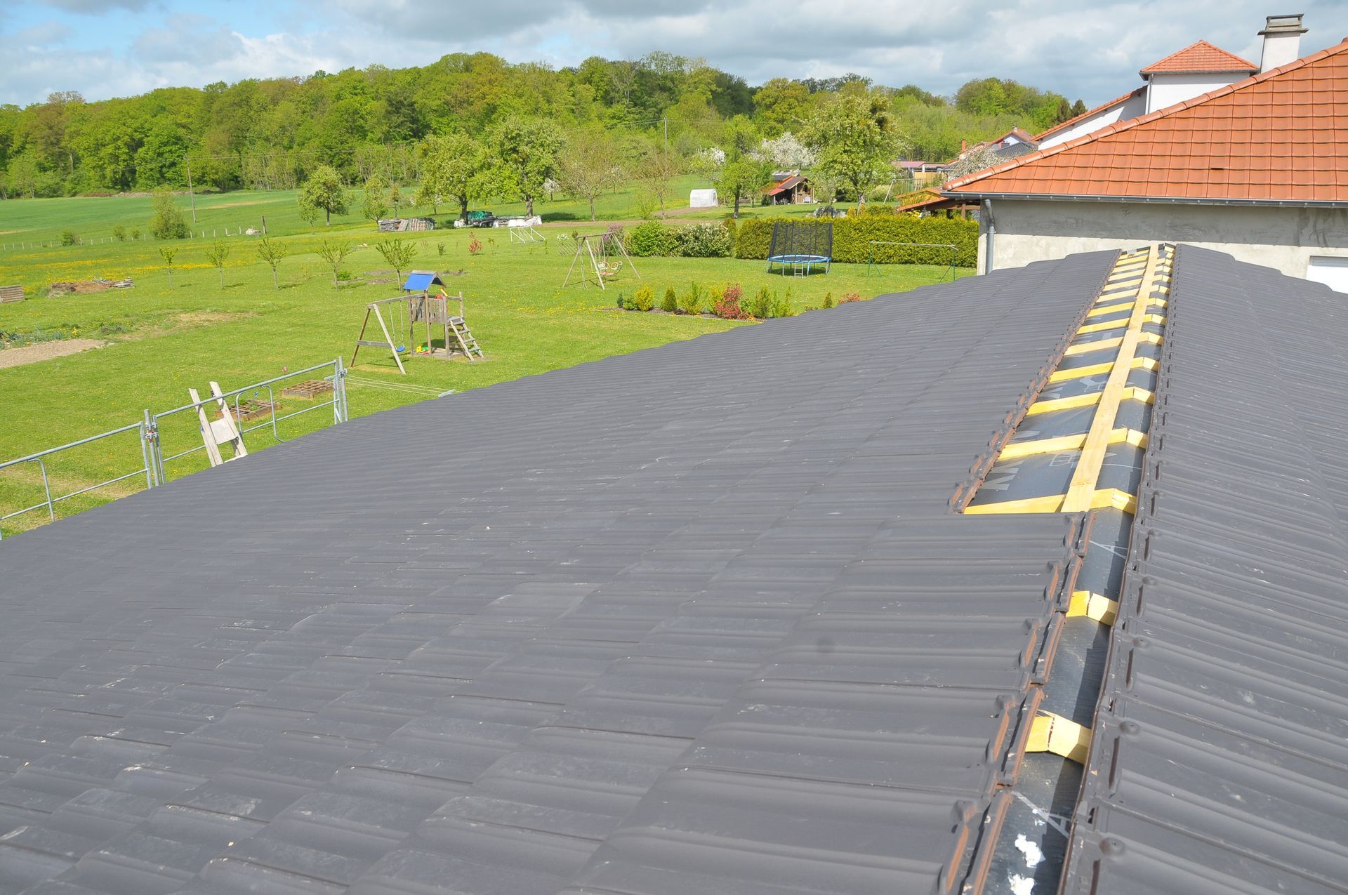 Toiture en tuiles gris foncé posée sur une charpente en bois.