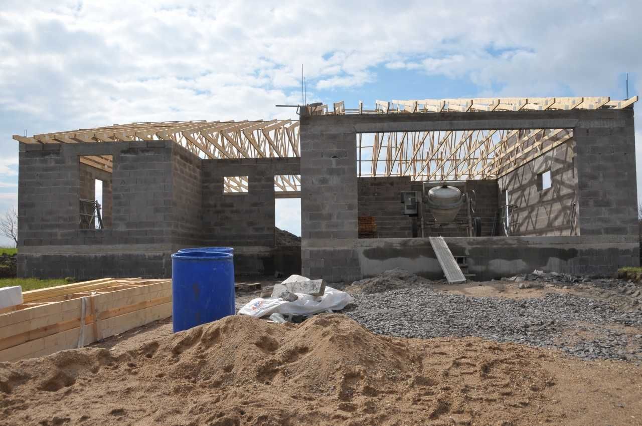 Construction d'un bâtiment de plain-pied avec murs et charpente apparents en parpaings, en extérieur.