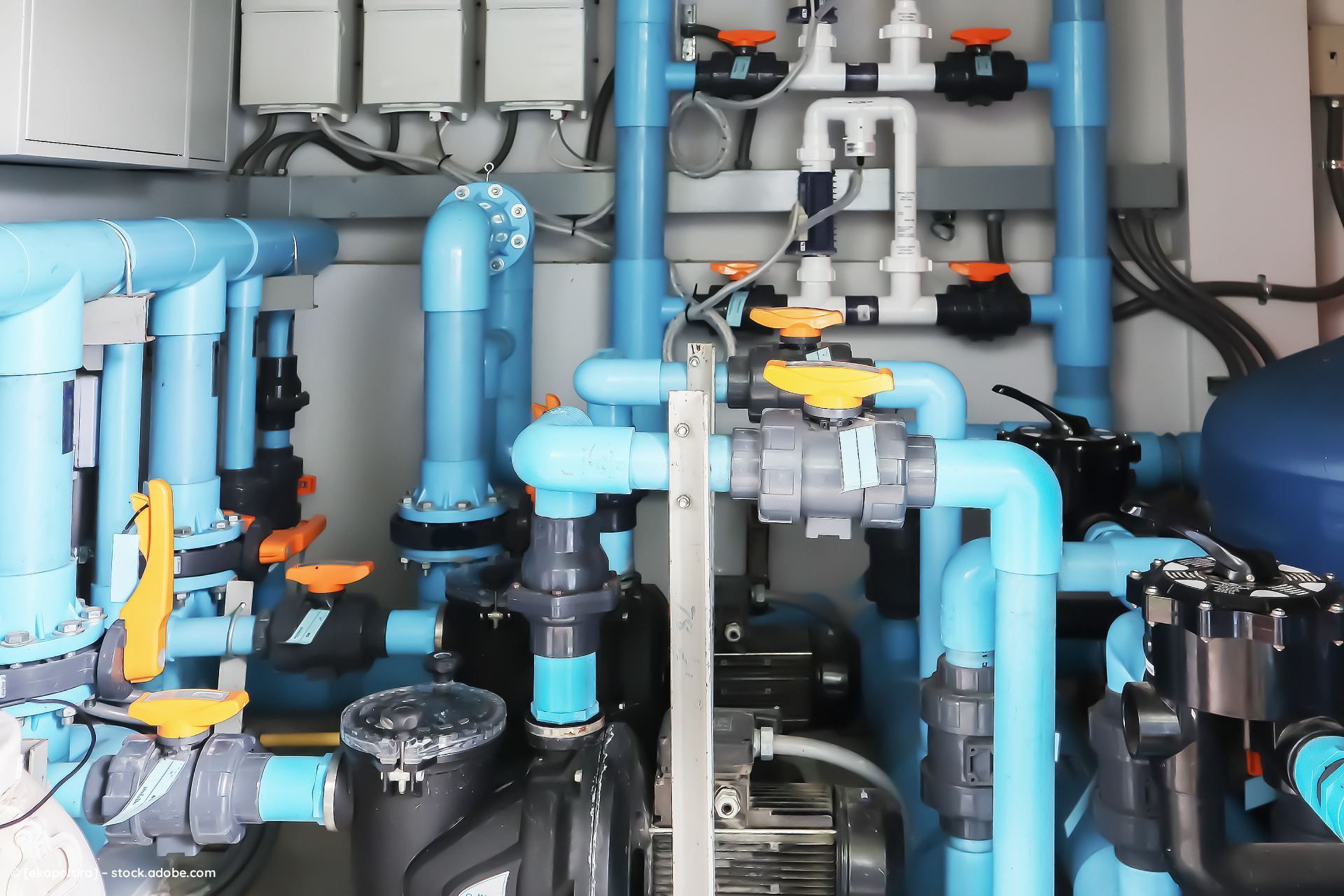 Ein komplexes System aus blauen PVC-Rohren, Ventilen und Industriepumpen zur Wasserfiltration oder -aufbereitung.