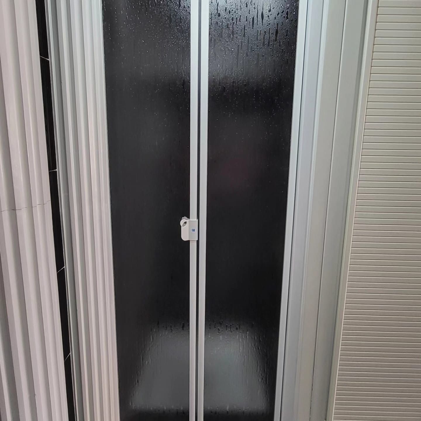 Una mampara de ducha con puertas de vidrio esmerilado, marcos blancos y manija plateada.