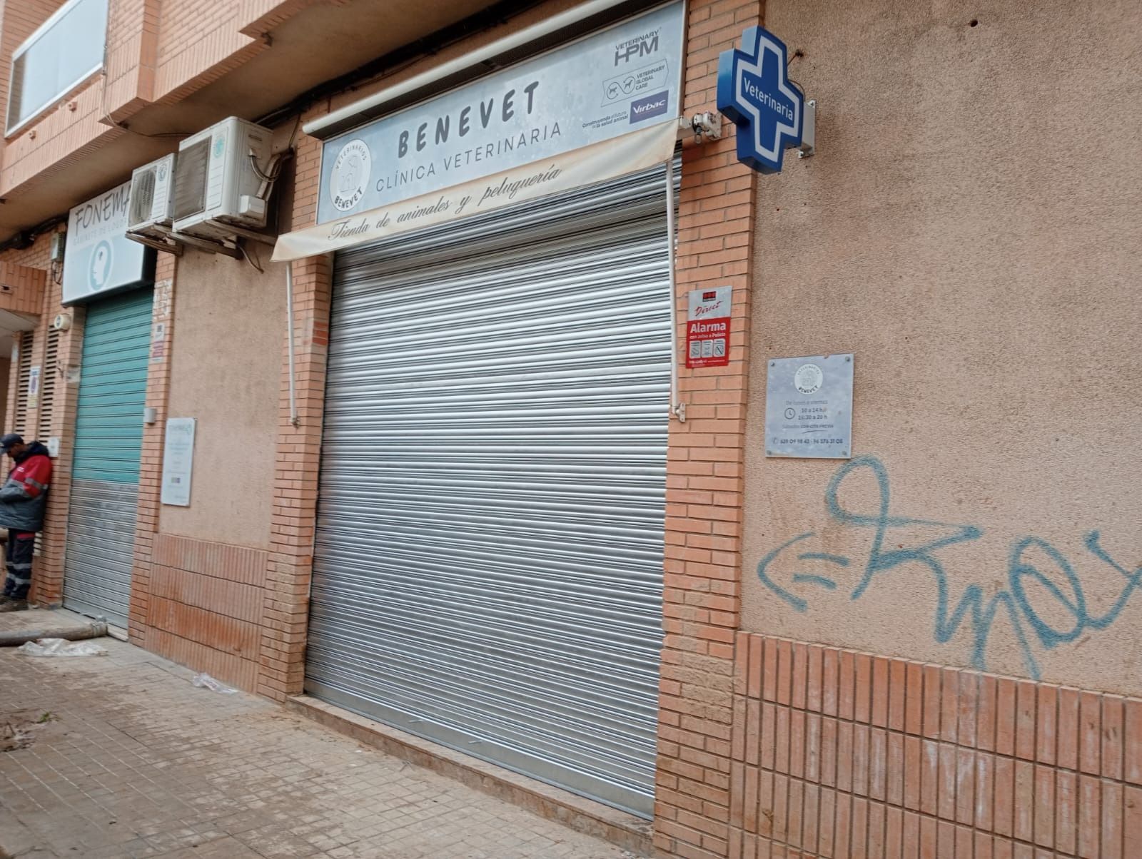 Clínica veterinaria cerrada con persiana metálica de seguridad y símbolo de cruz azul.
