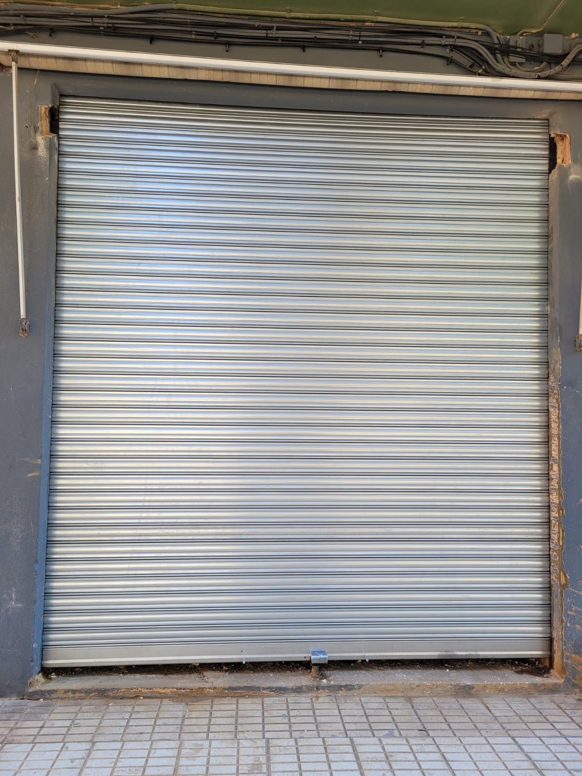 Persiana enrollable de metal plateado cerrada sobre la fachada de un edificio gris.