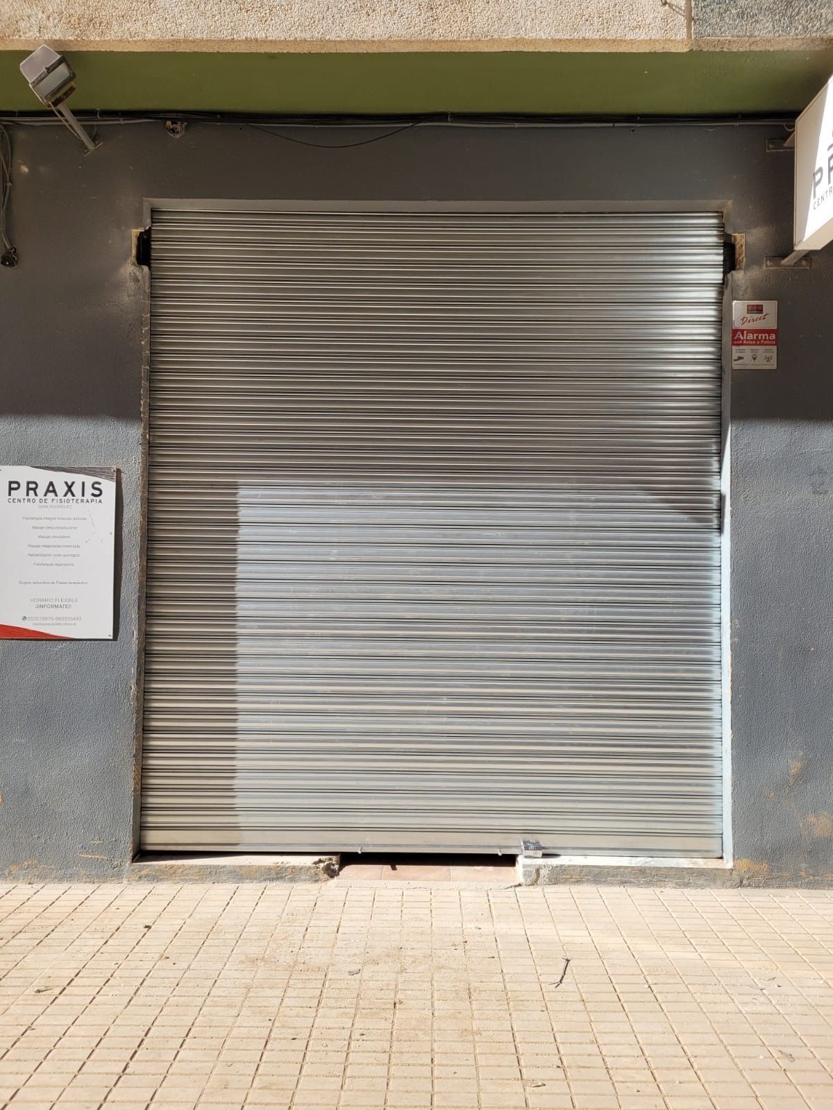 Escaparate metálico cerrado con cartel, sobre pavimento de ladrillo.