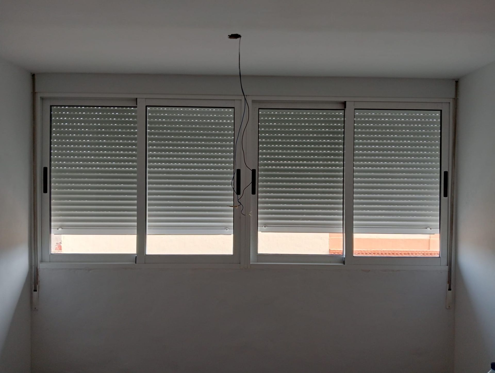 Ventana con persianas grises cerradas en una habitación con paredes blancas.