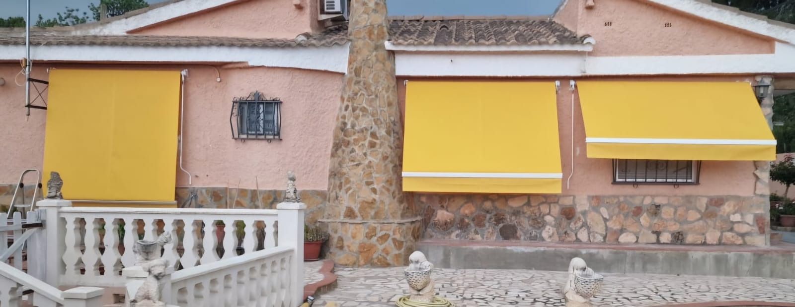 Una casa con toldos amarillos y un pilar de piedra. Hay una cerca blanca delante de la casa.