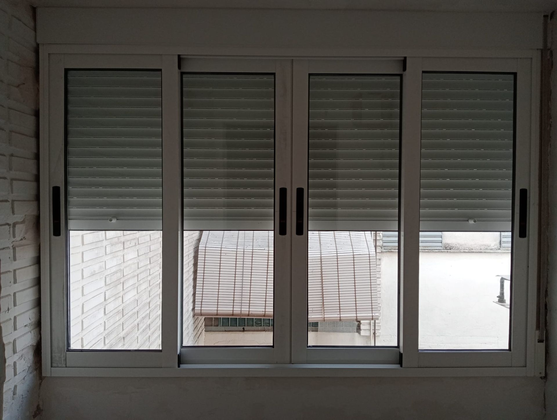 Ventana corrediza blanca con persianas cerradas, empotrada en una pared de ladrillo.