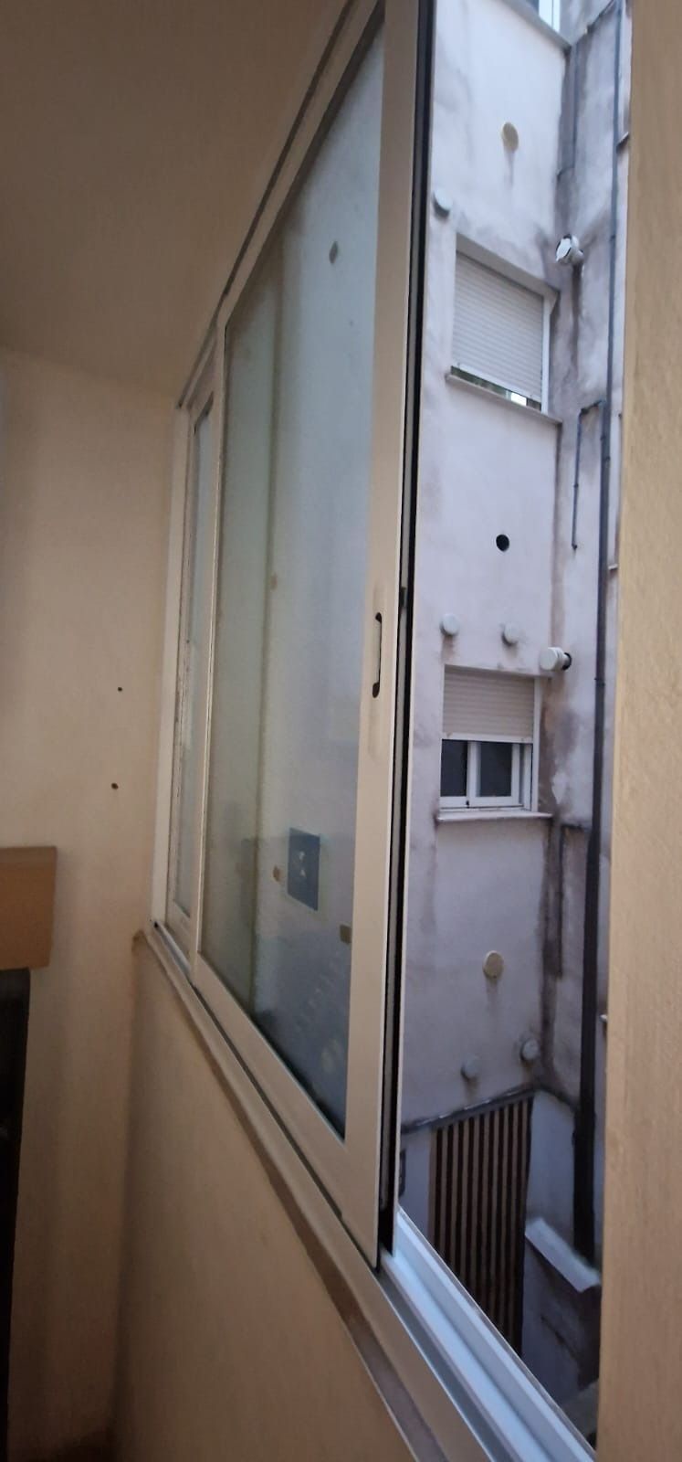 Ventana abierta con vista a un patio estrecho con un edificio de varios pisos.