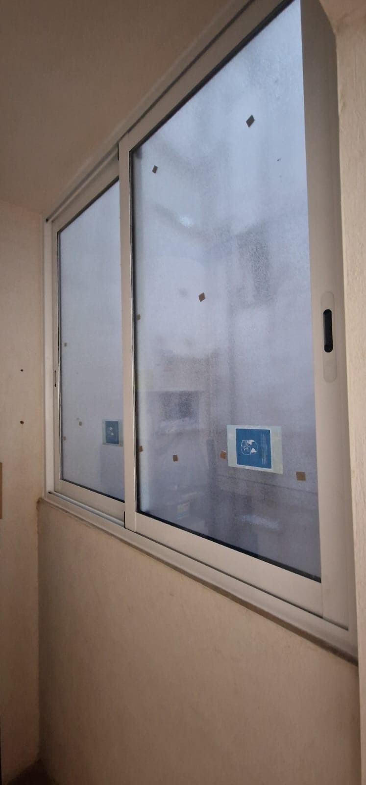 Una ventana corrediza de vidrio, dentro de una habitación de color claro, con un panel parcialmente abierto y pegatinas azules y blancas en el vidrio.