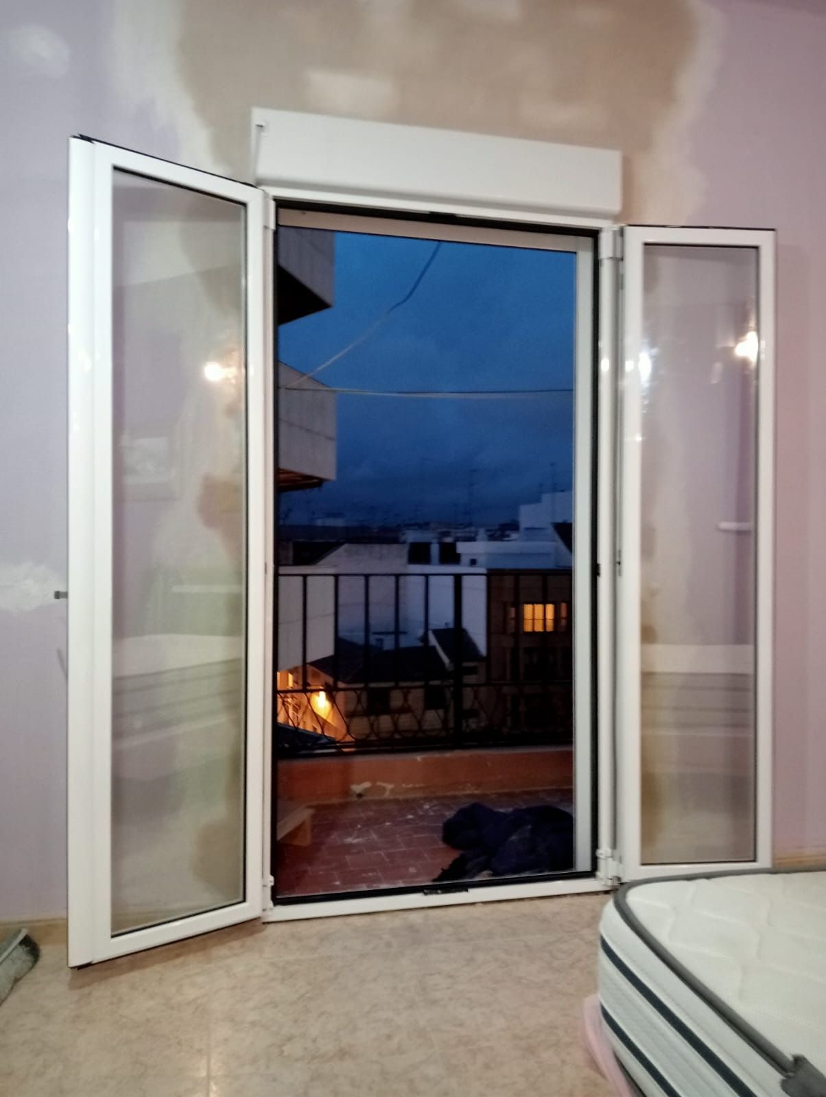 Puertas francesas blancas abiertas con vista al paisaje urbano al atardecer.