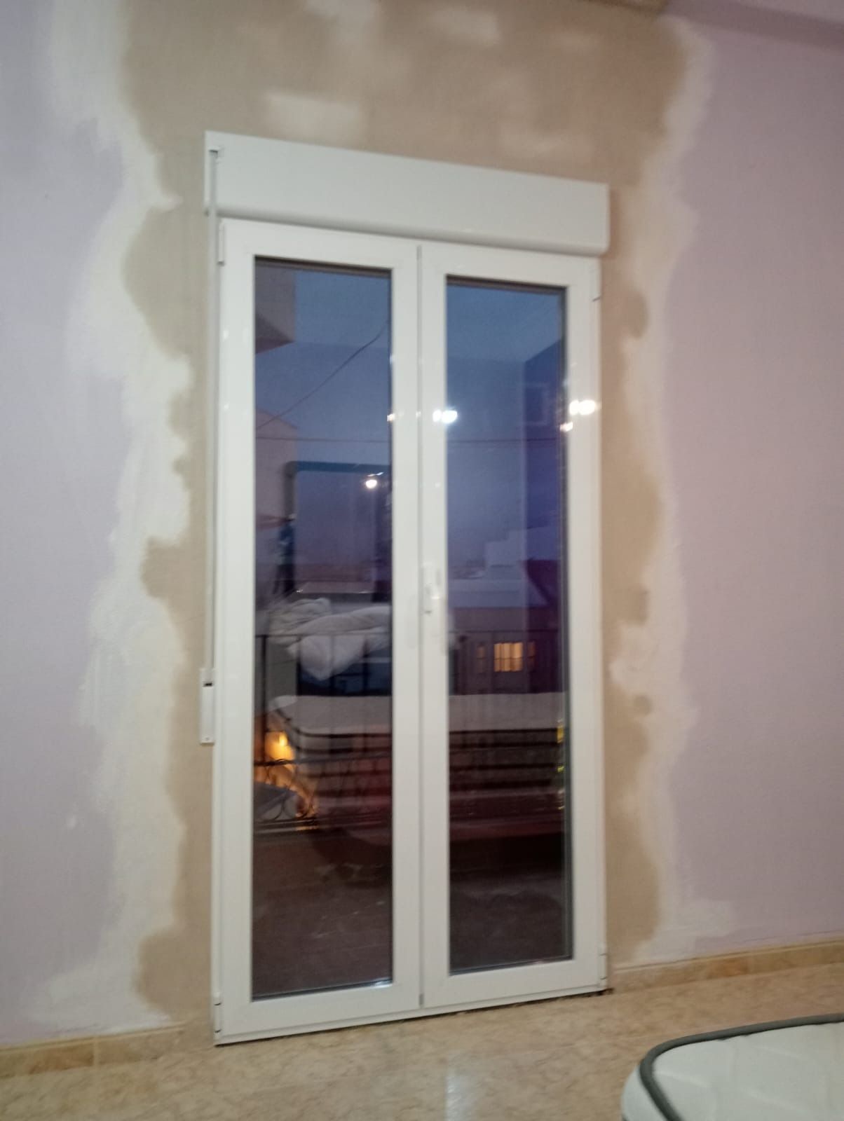 Puertas dobles de vidrio con marco blanco y persiana enrollable. Las puertas se encuentran en una habitación con paredes rosas y tostadas.