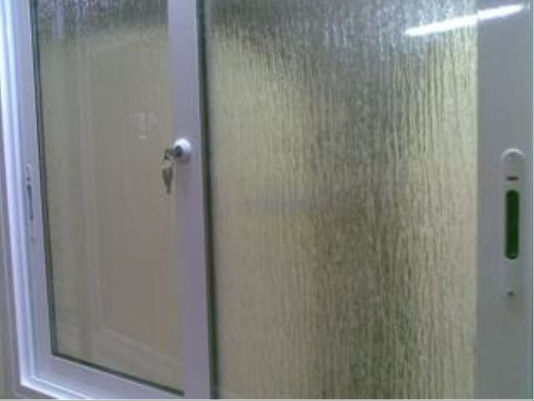 Ventana corrediza blanca con vidrio texturizado para privacidad, ligeramente abierta.